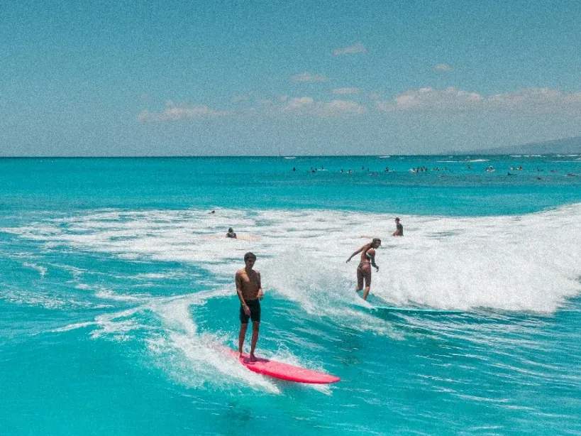 Two surfers riding a wave in turquoise water, one on a pink board
