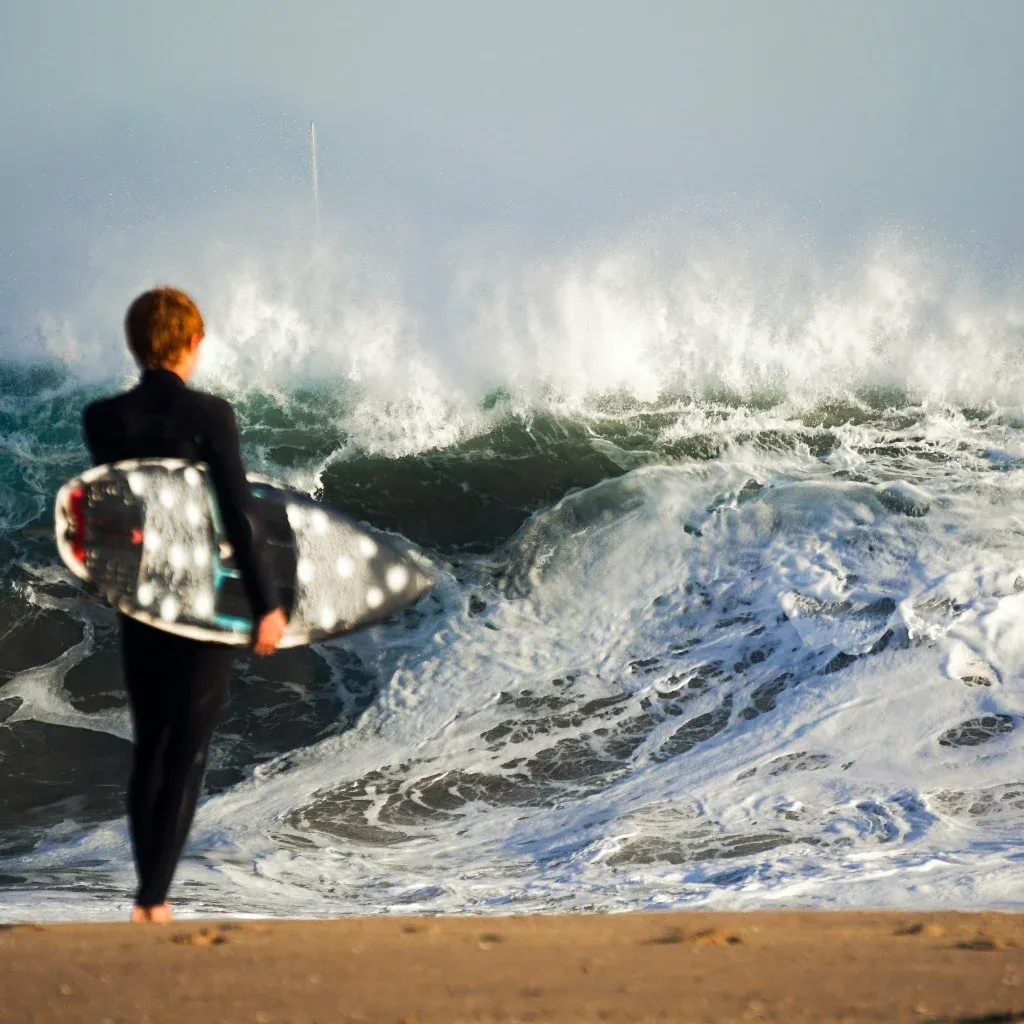 Surfer holding a board and watching a big wave break