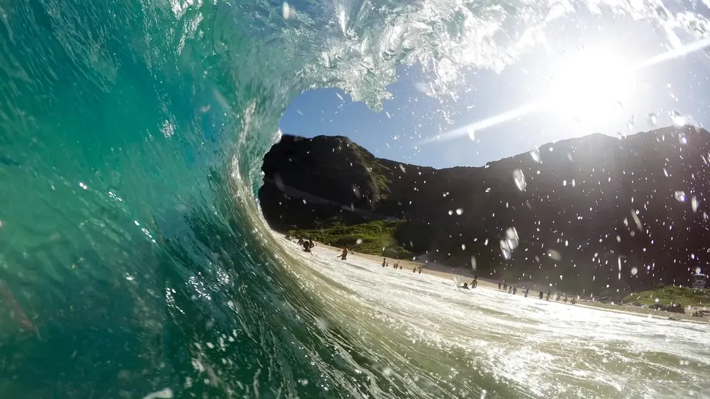 View from inside a breaking wave looking out at a beach and green hills