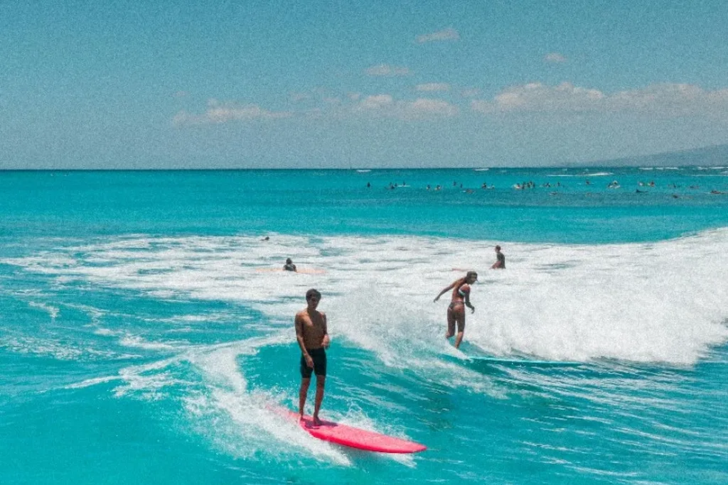 Surfers riding small turquoise waves under a clear sky