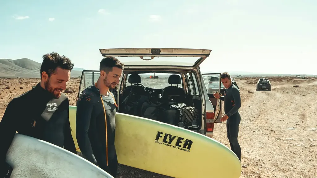 Surfers unloading boards from the back of a van on a sandy track