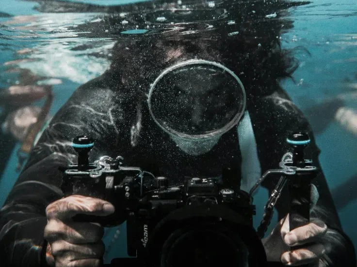 Water photographer underwater, holding a camera in a housing toward the lens