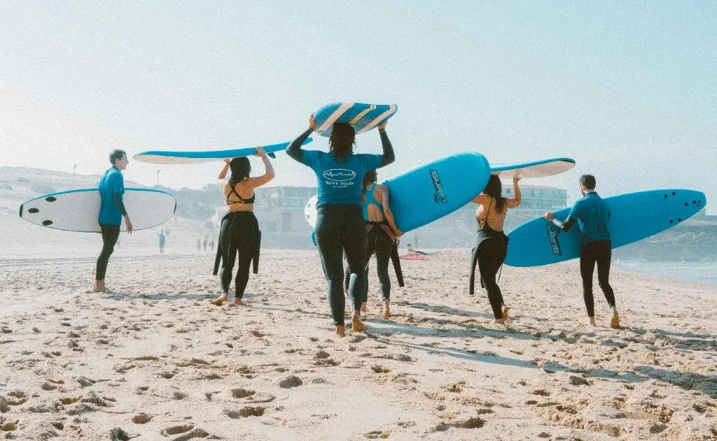 Surf school group walking down the beach carrying soft-top boards