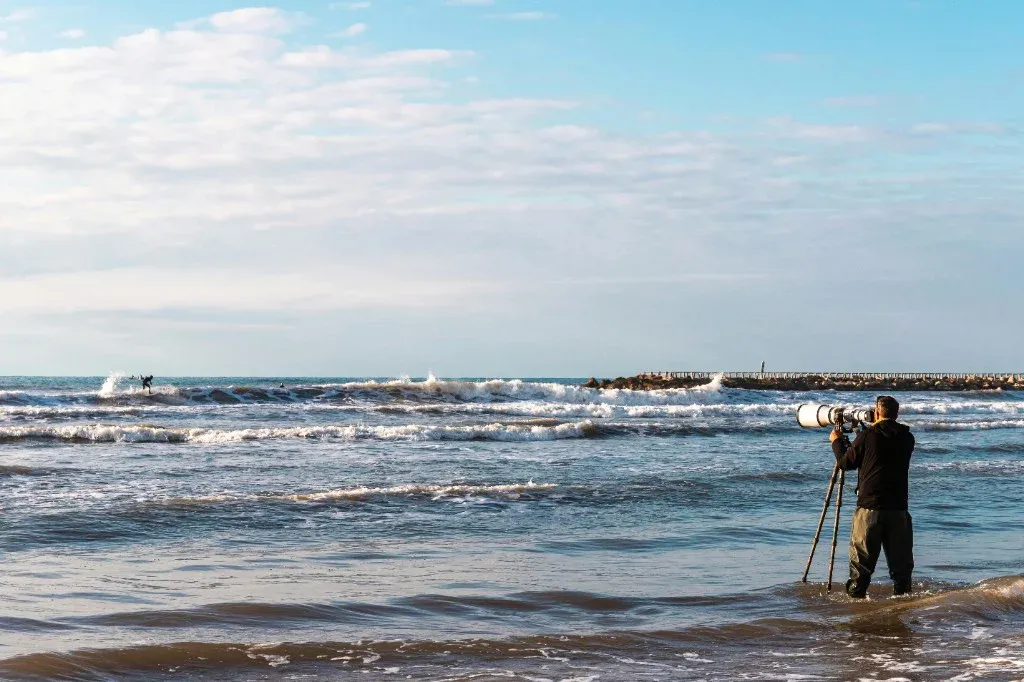 Photographer with a long lens on a tripod, standing at the water's edge